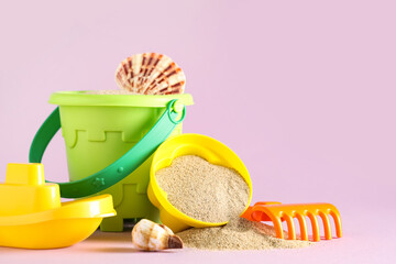 Seashells, sand, beach toy mold, ship, toy rake and bucket on pink background