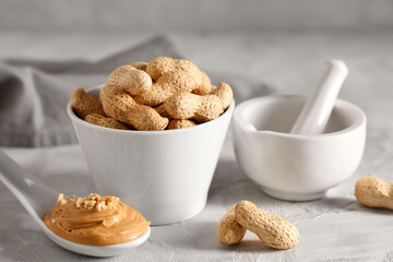 Spoon with peanut butter, bowl of nuts and mortar on light table