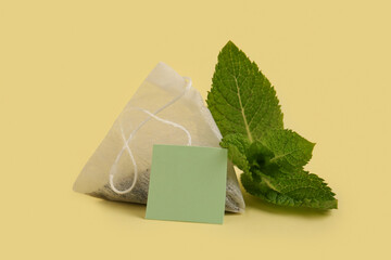 Composition with tea bag and mint leaves on yellow background, closeup
