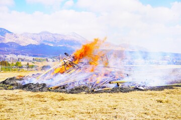 青空バックで崩れた燃えるどんど焼きの大きな櫓、新年の無病息災を願う日本の正月の風習