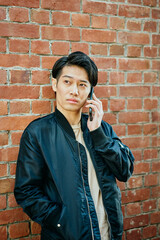 レンガの壁の前でスマホを操作する若い男性ポートレート