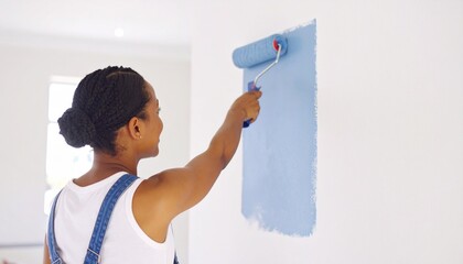 African woman applying a fresh coat of blue paint to a wall with a roller during a DIY home improvement project
