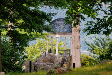 Historic neoclassical temple-style gazebo with ornate domed roof and stone columns perched on rocky outcrop surrounded by lush green foliage