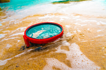A diving mask lies on a sandy beach and is washed by waves of water