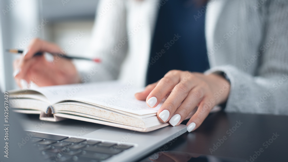 Poster student reading a book with laptop computer on table in university library, close up. business woman
