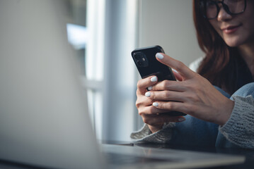 Close up, business woman using mobile smart phone with laptop computer on office table. Woman using smartphone searching the information, surfing the internet, social network