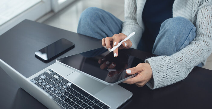 Young casual business woman sitting on the floor using stylus pen and digital tablet, working on laptop computer at home office. Female student online studying, E-learning
