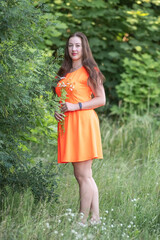 Portrait of a beautiful young plump girl in an orange dress in the forest.