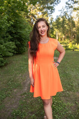 Portrait of a beautiful young plump girl in an orange dress in the forest.