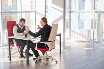 Two Caucasian men using smartphones while sitting at a desk. 