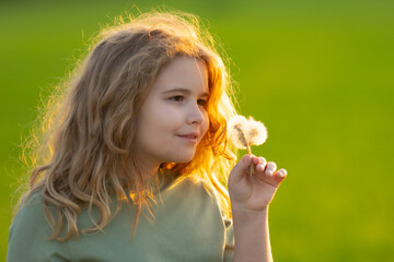 Cute blonde child face. Kid blows a dandelion on summer field. Kids portrait close-up. Kid with...