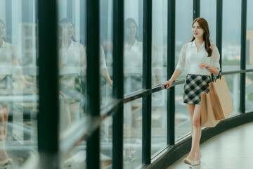 Smiling Asian woman carrying a shopping bag, enjoying her time in a casual outfit — capturing the joy of a carefree day out.