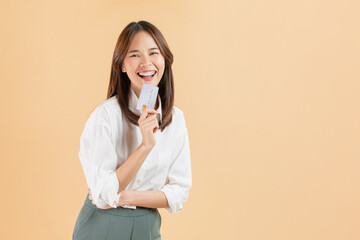 Cheerful beautiful Asian woman holding credit card isolated on beige color background.
