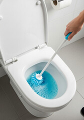 Hand cleaning a white toilet bowl with blue water and a brush