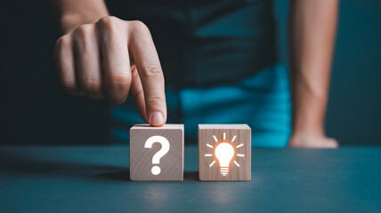 Fingers point from question mark to lightbulb on wooden blocks, symbolizing transition from problem to solution or idea generation.