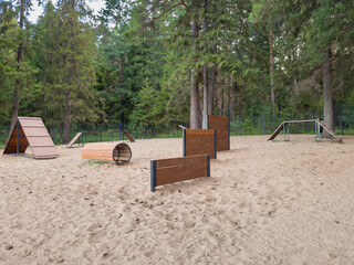 Outdoor dog agility training area featuring various obstacles like tunnels, ramps, and barriers,...