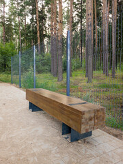 Wooden bench made of natural materials is placed along a walking path in a serene forest setting,...