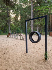 Outdoor playground featuring a tire swing hanging from a sturdy frame, surrounded by sandy ground and wooden climbing structures, inviting children to play and explore nature