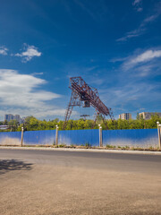 Industrial crane structure stands tall against a clear blue sky, surrounded by greenery and urban...