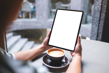 Mockup image of a woman holding digital tablet with blank white desktop screen in cafe