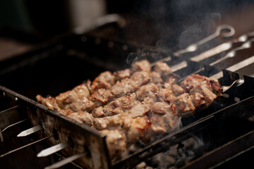 Grilled meat skewers cooking on metal barbecue grill with smoke rising from hot charcoal during...
