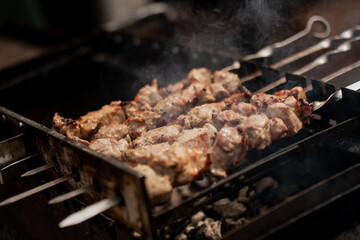 Grilled meat skewers cooking on charcoal grill with smoke rising in close-up view, traditional barbecue preparation with metal skewers over open fire during summer cookout