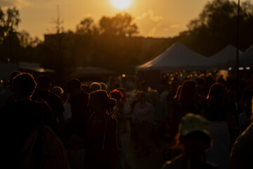 Crowd of people at outdoor festival during golden sunset, silhouettes and warm light create vibrant...