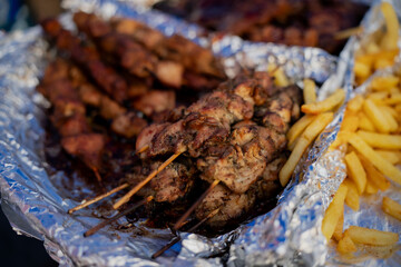Grilled meat skewers with crispy french fries served on foil at outdoor market, popular street food meal for barbecue, takeaway, catering, event or fast casual dining themes