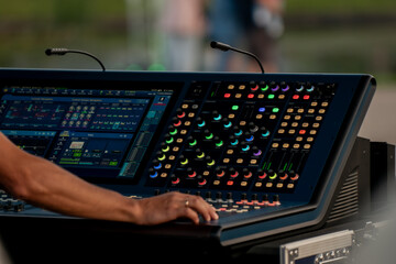 Close-up of professional audio engineer operating colorful digital sound mixing console at live...