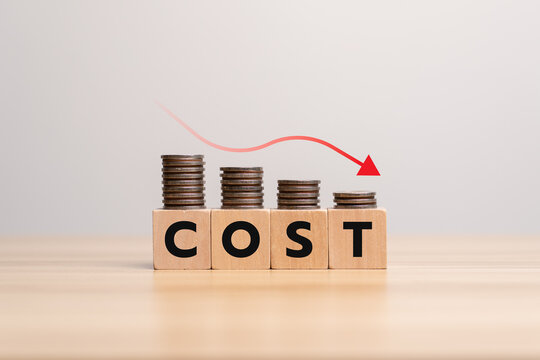 Concept of cost reduction in business finance with wooden blocks spelling COST placed on descending stacks of coins, red downward arrow, symbolizing decreasing expenses, saving strategy, efficiency