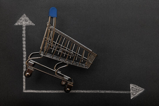 Empty miniature supermarket shopping cart on chalk drawn financial chart background