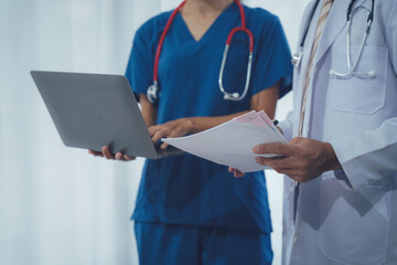 Medical Professionals in Collaboration: Two medical professionals are deep in consultation, examining a report and laptop, representing healthcare teamwork, medical expertise.