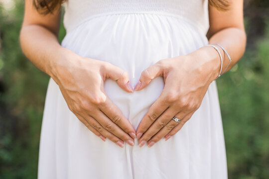 a woman making a heart with her hands on her pregnant belly