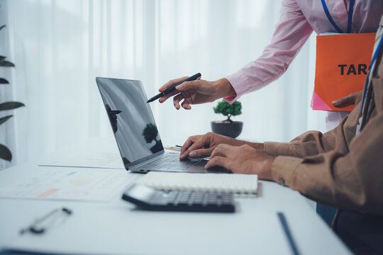 Tax Consultation Collaboration: An advisor offers guidance as a person delves into tax paperwork, symbolized by a laptop computer. The setting is a business context.