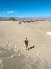 Sunlit overhead view of a teenage girl walking alone through sand dunes in Death Valley, USA, back to camera under clear skies.