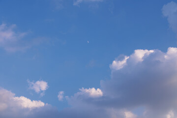 Dramatic sky with blue tones, fluffy white clouds, dark storm clouds, and a visible daytime moon. Peaceful yet moody natural sky background.