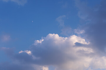 Dramatic sky with blue tones, fluffy white clouds, dark storm clouds, and a visible daytime moon. Peaceful yet moody natural sky background.