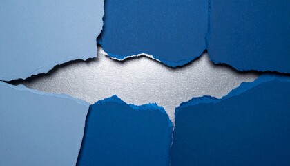 A creative composition of ripped blue paper in various shades, forming a jagged gap that reveals a shiny silver background.