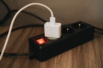 White Charger Plugged Into Black Power Strip On Wooden Surface