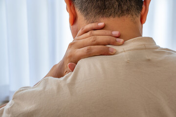 Asian man grasping left neck in discomfort after long work hours—medical concept for muscle...