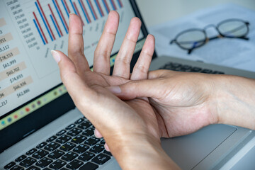 Close-up of hands massaging wrist over laptop—sign of digital strain, carpal tunnel, or...