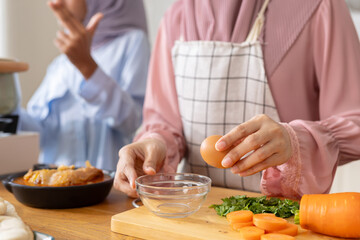 Close up hand highlighting act of cracking fresh raw egg into bowl to cook amidst freshly chopped vegetables and comforting dishes. Family members enjoy quality time in warm kitchen preparing meal.