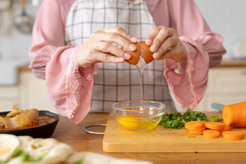 Close up hand highlighting act of cracking fresh raw egg into bowl to cook amidst freshly chopped...