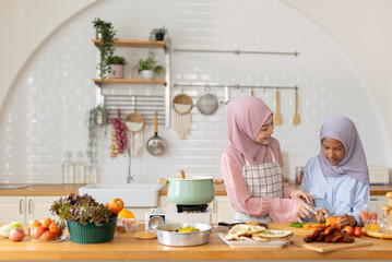 Joyful cooking session lifestyle in contemporary kitchen, Muslim women and girl of different ages in hijabs chop fresh vegetables and prepare meal amidst colorful ingredients and kitchenware.