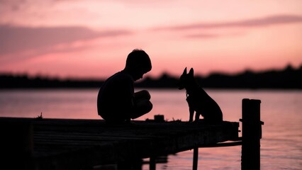 Silhouette of a boy and dog on a pier at sunset