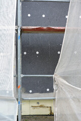 A wall of a house covered with EPS graphite polystyrene boards for thermal insulation, a scaffolding and building safety scaffolding net, anchors