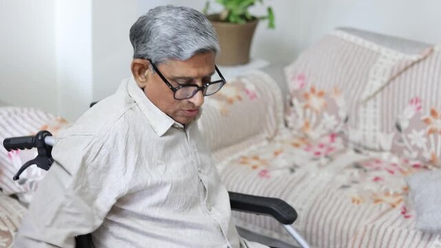 Senior disable indian man sitting on wheelchair at home. Elderly person healthcare. 4k
