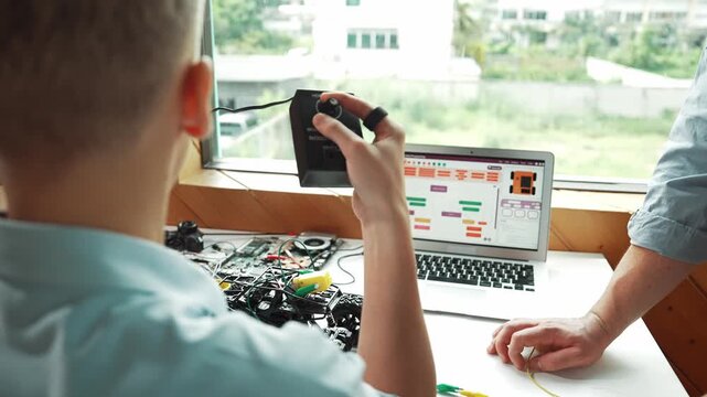 Back view of smart student learning about car model controller while teacher giving advise at table with laptop display coding engineering prompt or programming system screen at STEM. Edification