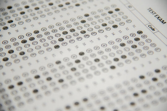Here is a description of the image in English:

This is a close-up, angled shot of a paper multiple-choice answer sheet, often called a "bubble sheet." It shows numbered questions down the side (1, 2,