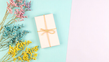 Soft pastel gift box tied with twine on blue and pink background with colorful dried flowers, creating delicate and charming aesthetic perfect for celebration or birthday mood